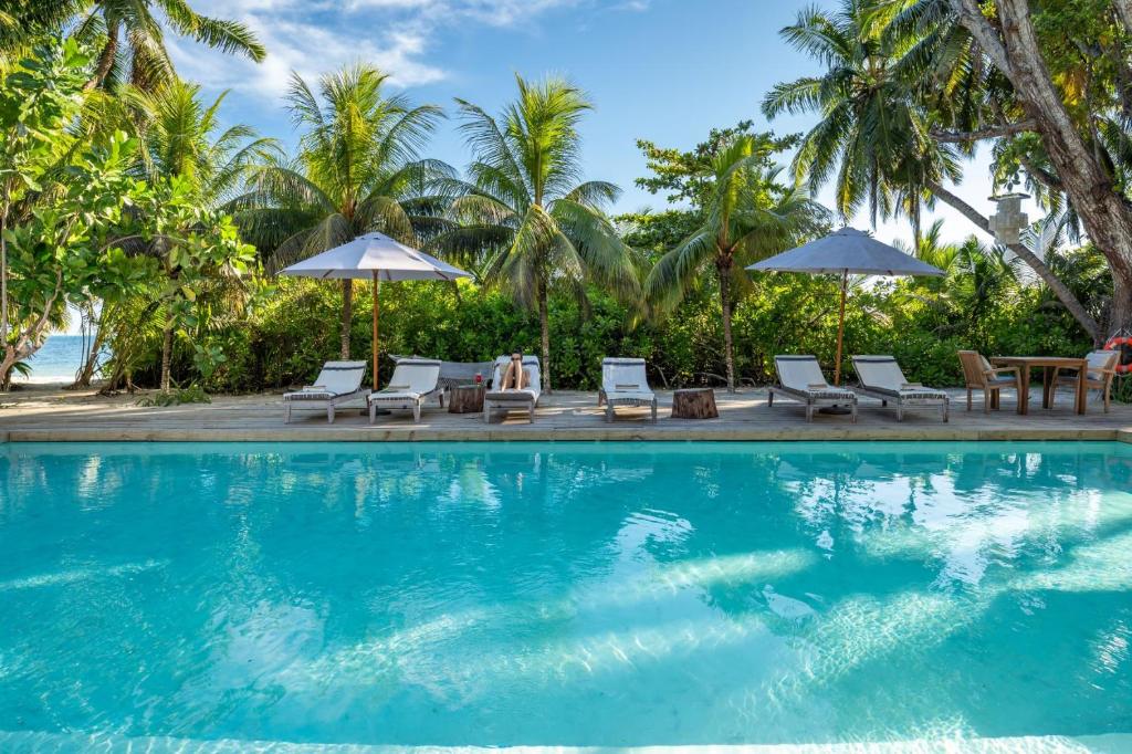 a swimming pool with chairs and umbrellas next to the ocean at Bliss Hotel Praslin in Grand'Anse Praslin