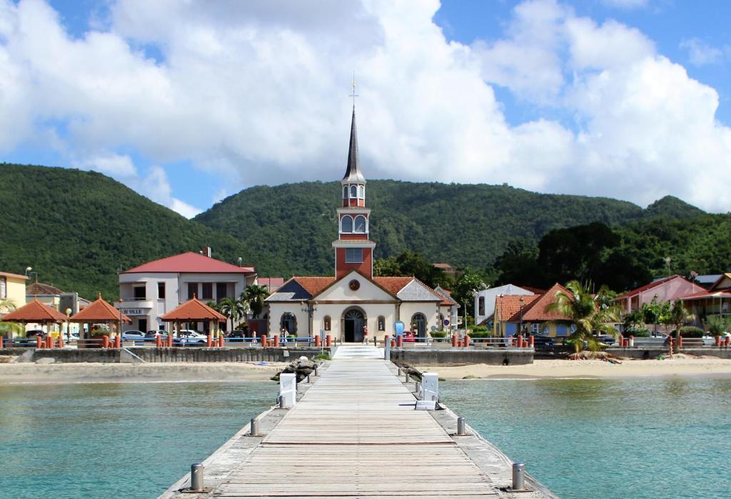 a church on the beach with a pier and water at Le COLIBRI in Les Anses-dʼArlets