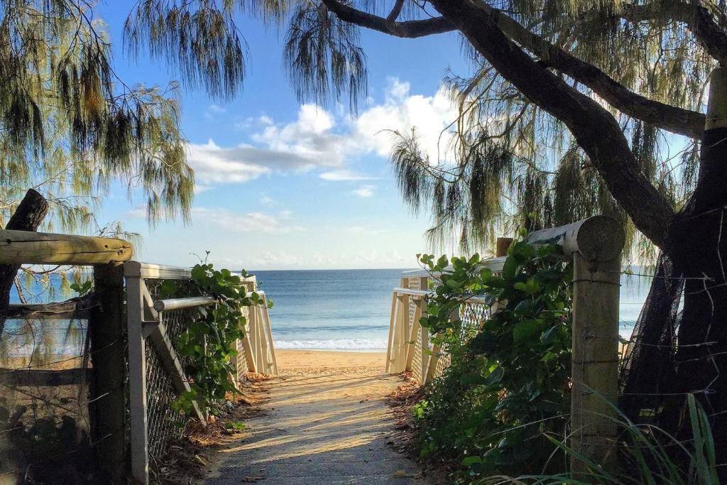 un chemin menant à la plage avec une clôture et un arbre dans l'établissement 20 Steps to the Sand!, à Mooloolaba