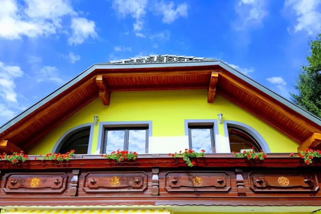 Una casa amarilla con ventanas y flores. en Rooms Močilnik, en Begunje na Gorenjskem