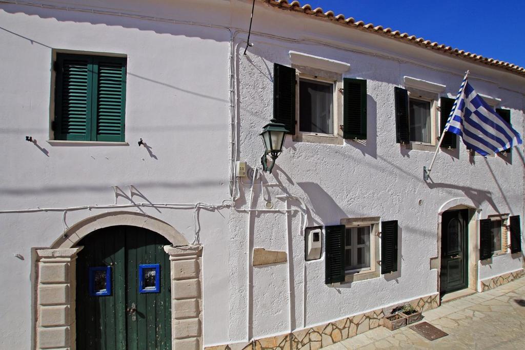 a white building with a green door and a flag at Archontiko Kourkoulos in Makrádes