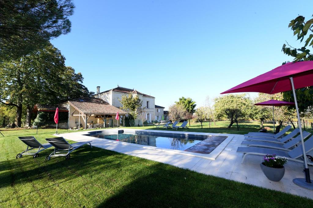 a backyard with a swimming pool with chairs and an umbrella at Belle demeure familiale avec piscine proche St Emilion in Bossugan