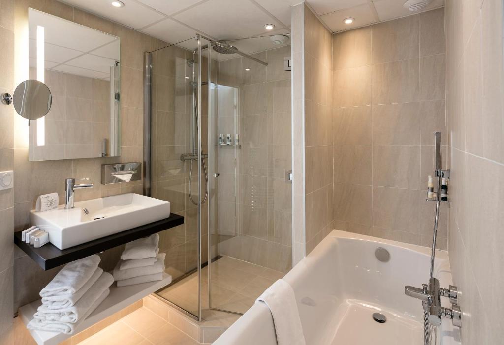 a bathroom with a shower and a sink and a tub at Thalazur Ouistreham - Hôtel & Spa in Ouistreham