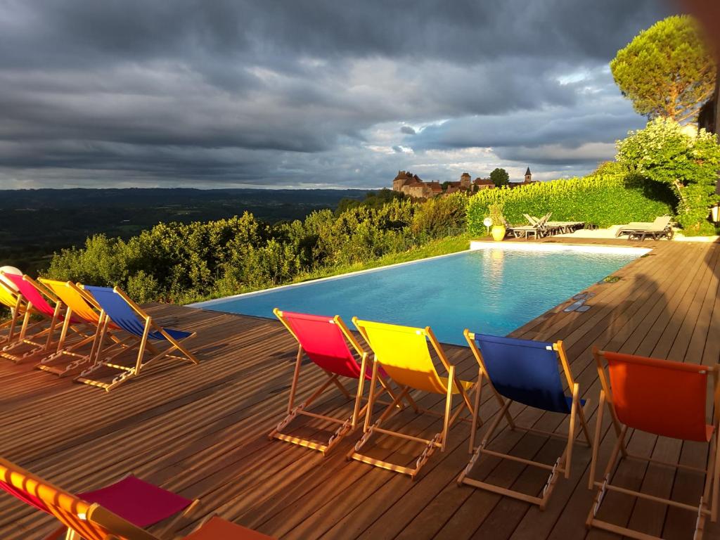 a group of chairs sitting on a deck next to a swimming pool at Le Relais de Castelnau in Loubressac
