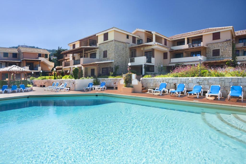 une piscine avec des chaises bleues et un bâtiment dans l'établissement Residence Bougainvillae, à Porto Cervo