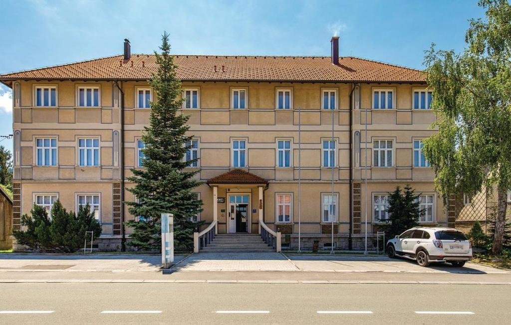 un grand bâtiment avec une voiture garée devant lui dans l'établissement Apartments and Rooms kod Eli, à Ravna Gora