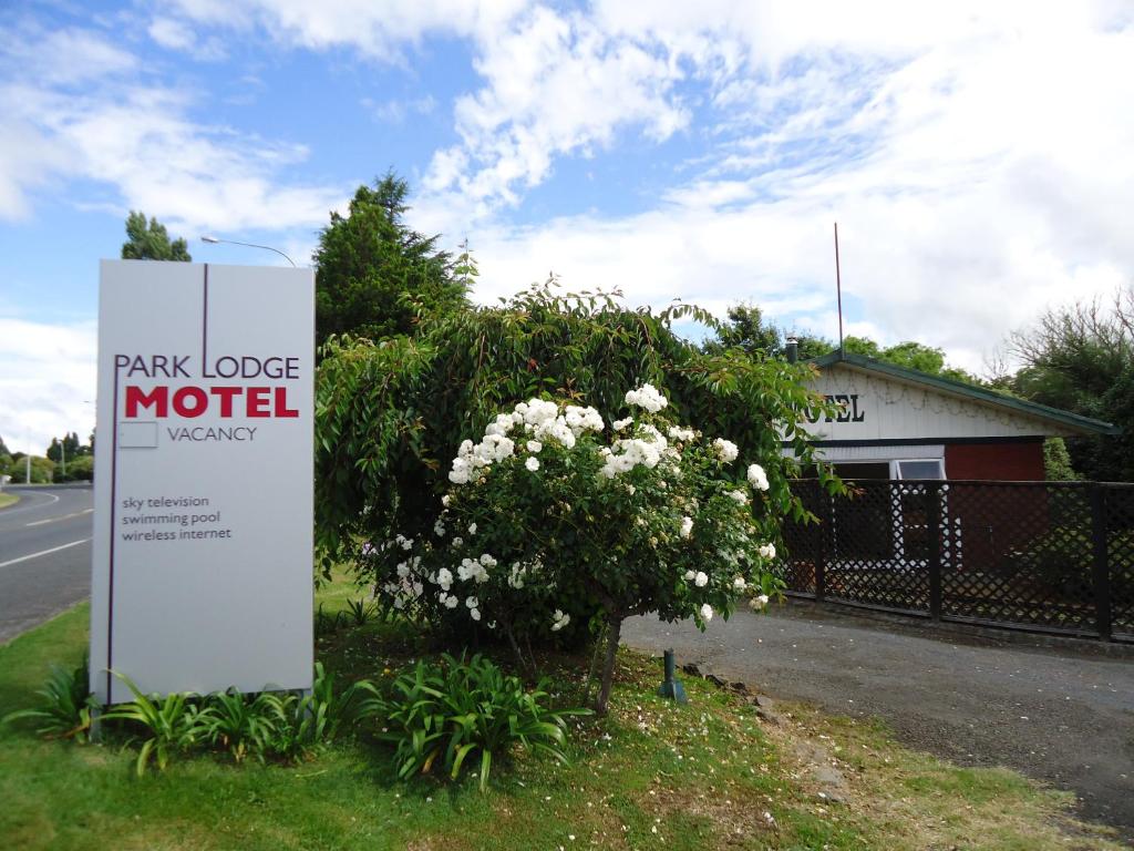 a sign for a motel next to a bush with flowers at Park Lodge Motel in Te Awamutu