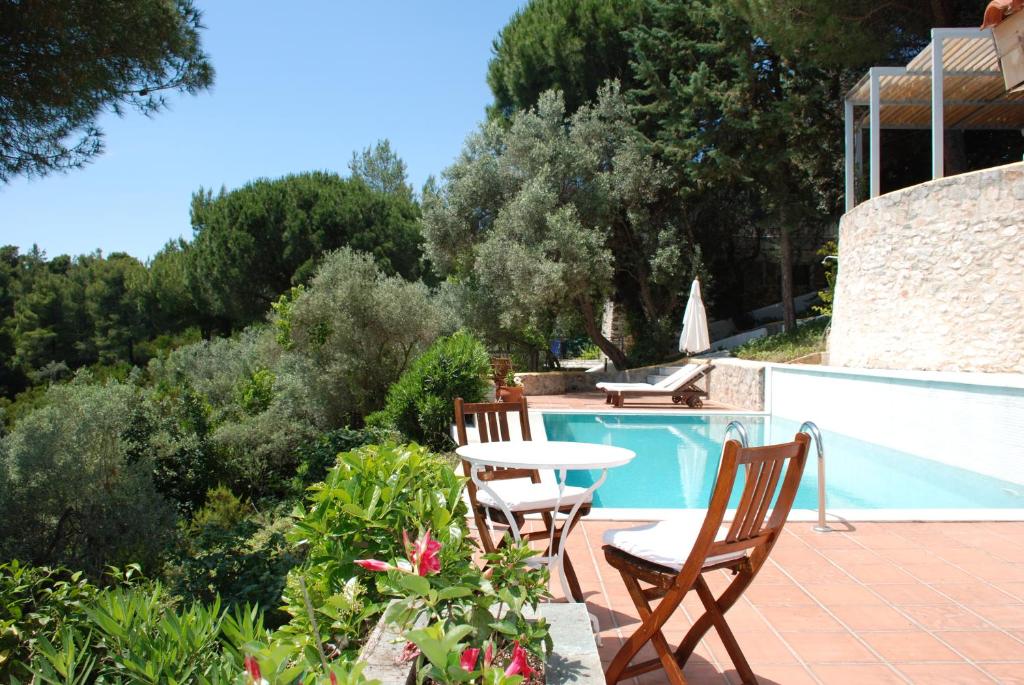 een patio met 2 stoelen en een tafel naast een zwembad bij VILLA ISMINI, Skiathos in Skiathos-stad