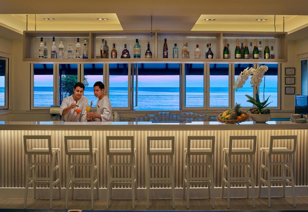 two people standing at a bar with the ocean in the background at Dusit Thani Laguna Phuket in Bang Tao Beach