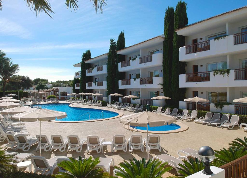 un hotel con piscina, sillas y sombrillas en Inturotel Esmeralda Garden en Cala d´Or