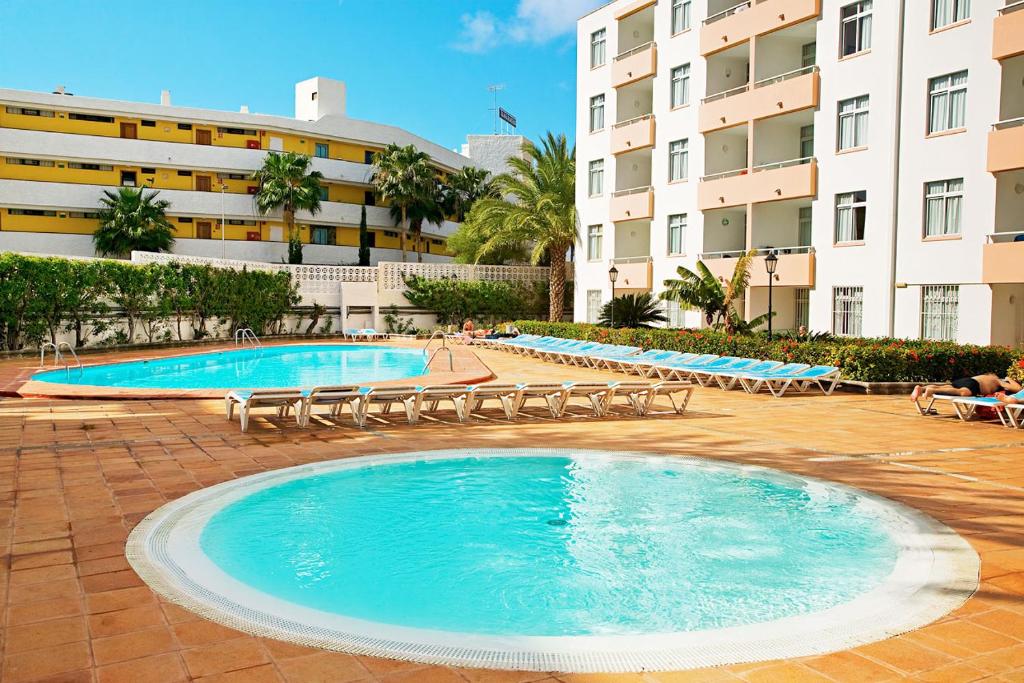 a large swimming pool with lounge chairs and a building at Farilaga Apartments in San Bartolomé