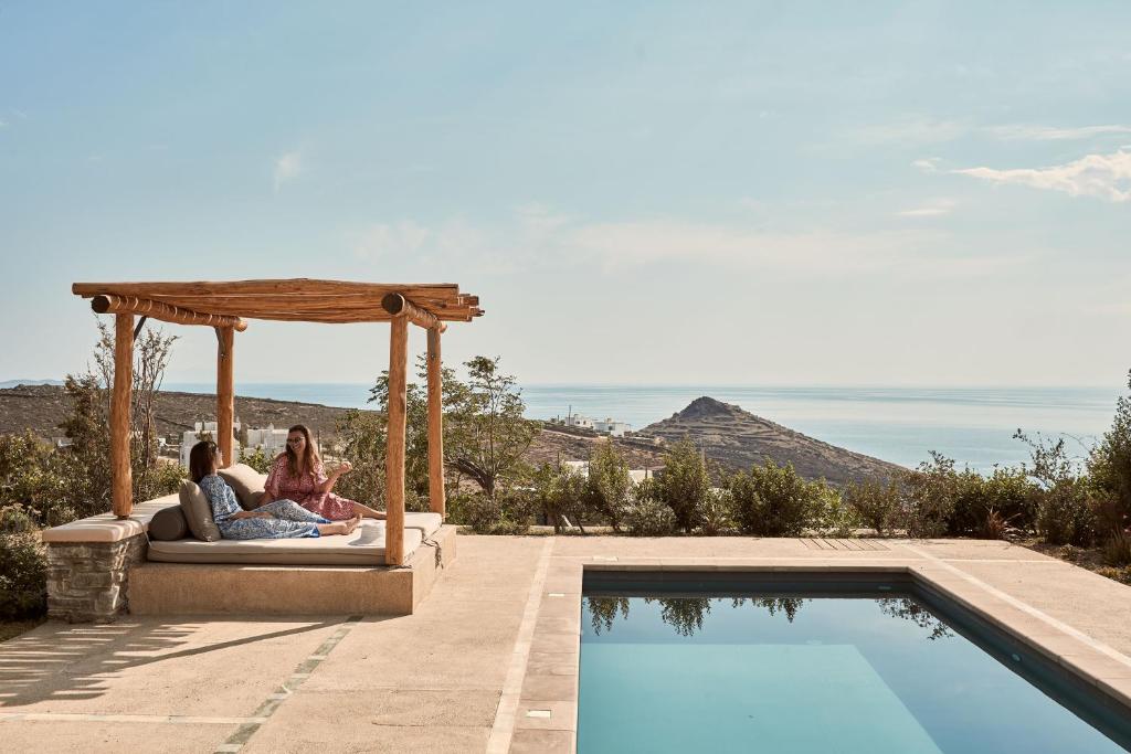 two women sitting on a bed next to a swimming pool at Diles & Rinies in Tinos