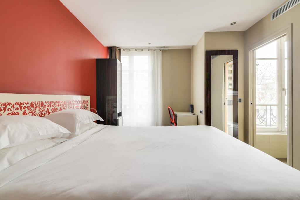 a bedroom with a large white bed with a red wall at Pavillon Nation in Paris