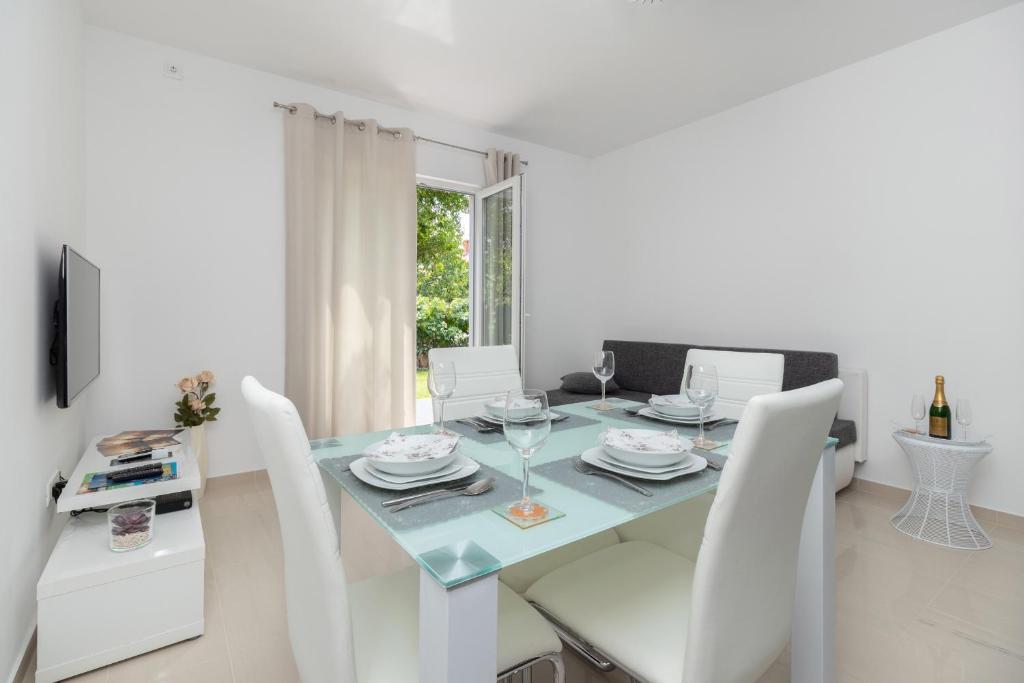 a white dining room with a glass table and white chairs at Apartments Peca in Zadar