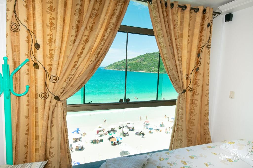 a bedroom with a window with a beach view at Loft da Prainha Resort AA 607 in Arraial do Cabo