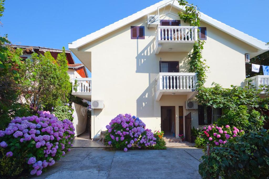een wit gebouw met paarse bloemen ervoor bij Apartments Ratković in Tivat