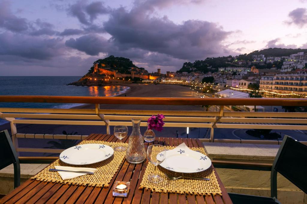 a table with plates and glasses on a balcony with the ocean at Edificio Tropicana in Tossa de Mar
