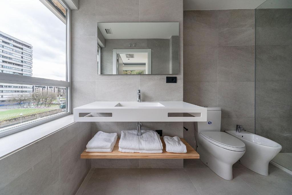Un baño con lavabo, inodoro y espejo. en Hotel Distrito Oeste, en San Sebastián