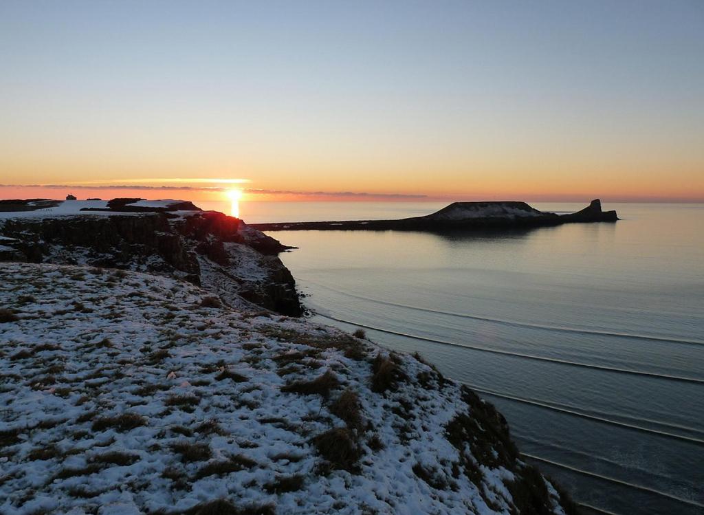 a sunset over a body of water with snow on the shore at King's Head Inn in Llangennith