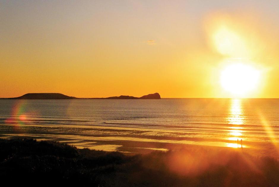 a sunset on a beach with the ocean at King's Head Inn in Llangennith