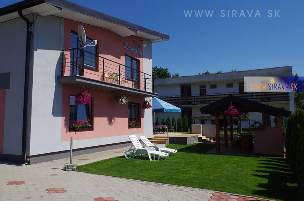 a pink building with two white chairs in a yard at Chata Zemplin in Kaluža