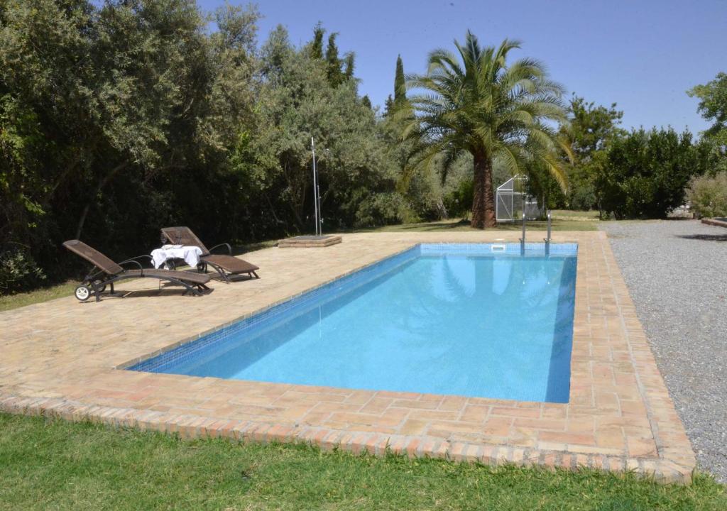 a swimming pool in a yard with two chairs at Cortijo Algabia in Alhendín