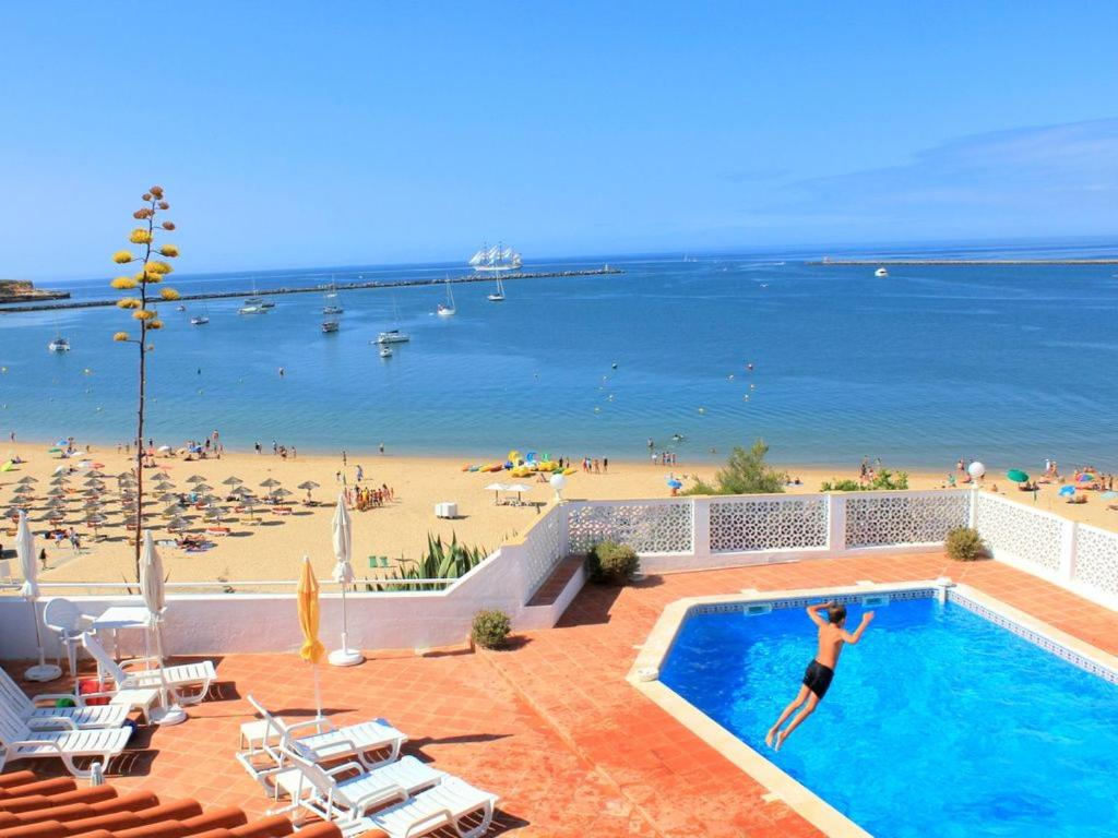 a person jumping into a swimming pool next to a beach at Vila Monte Luz 3 in Ferragudo