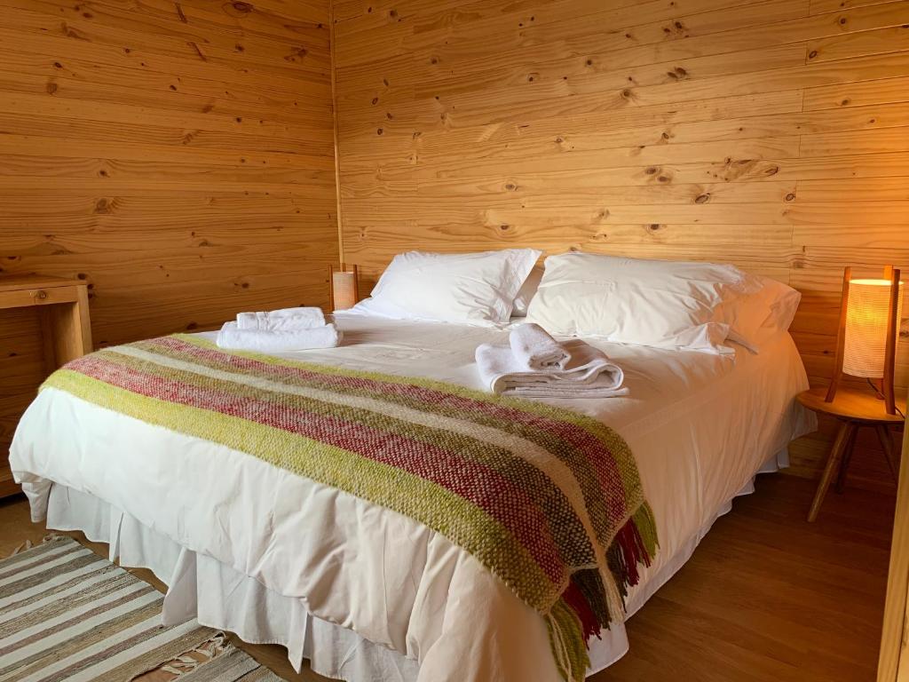 a bedroom with a white bed with a wooden wall at El Arrayan in Puerto Guadal