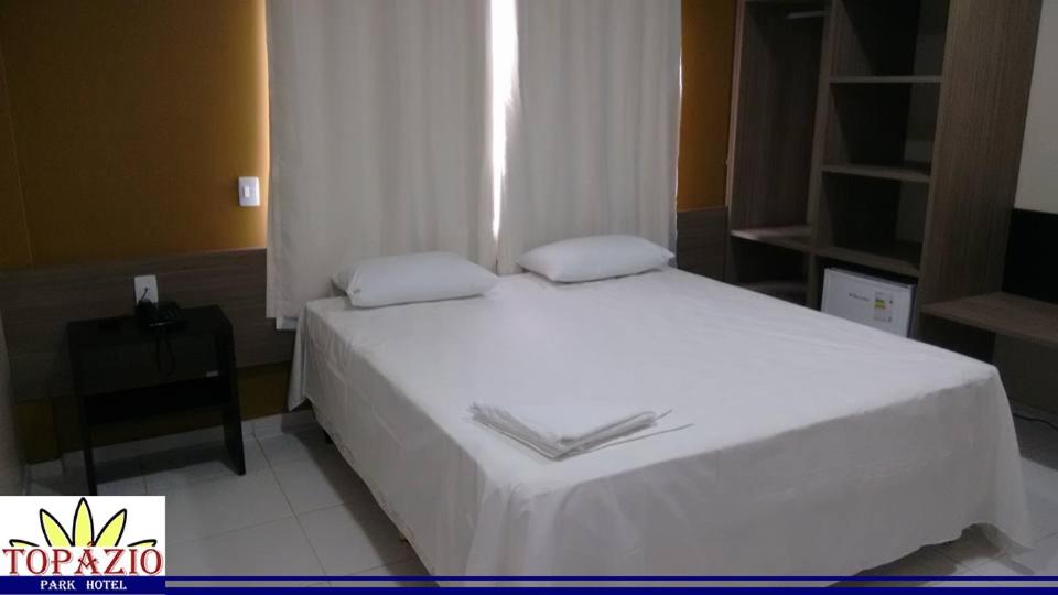 um quarto com uma cama com lençóis brancos e uma janela em Topázio Park Hotel em Afrânio