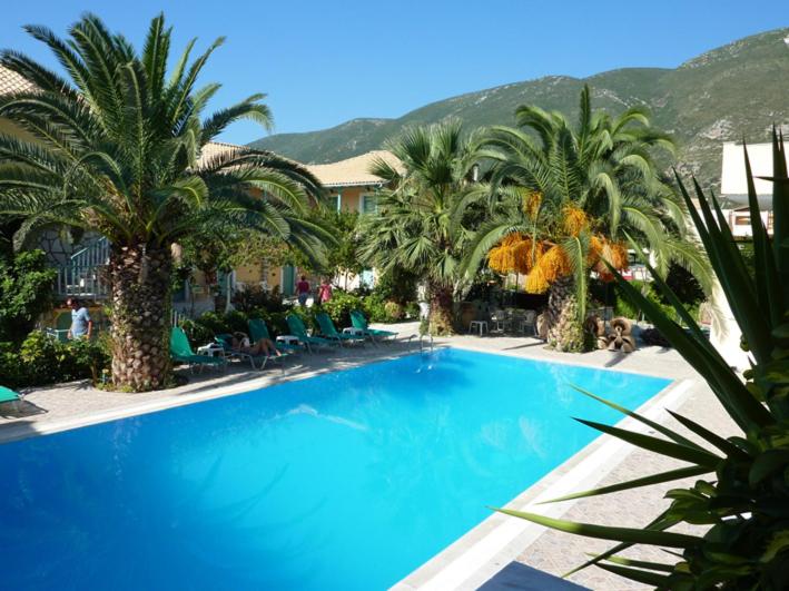 a large blue swimming pool with palm trees and chairs at Stavlos Cottage in Vasiliki