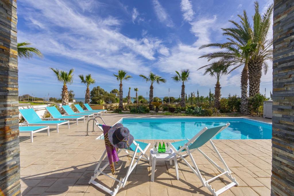 a pool with chairs and a table next to a swimming pool at Faros BeachFront Villa in Perivolia