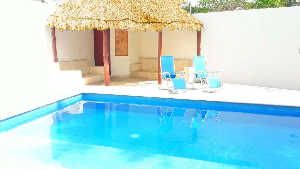 a pool with two blue chairs and a straw umbrella at Airport Bed and Breakfast in Cancún