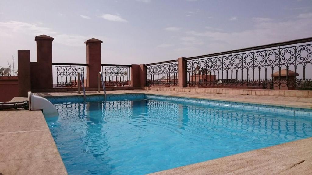 a swimming pool with blue water in front of a fence at Appartment Jnane Atlas in Marrakech