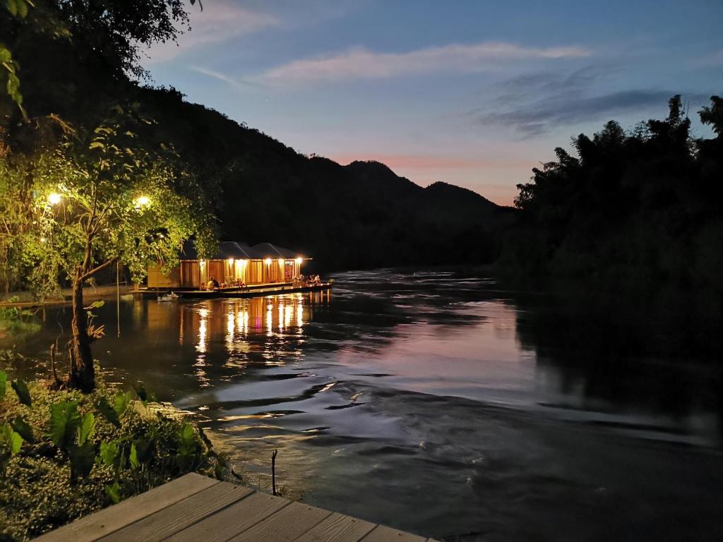 um barco com luzes sobre ele em um rio à noite em Kodaun River Kwai Resort em Kanchanaburi