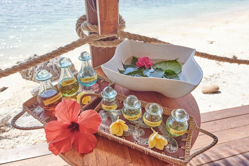 a tray with bottles of oil and a bowl of flowers at Cocotinos Sekotong Lombok in Sekotong