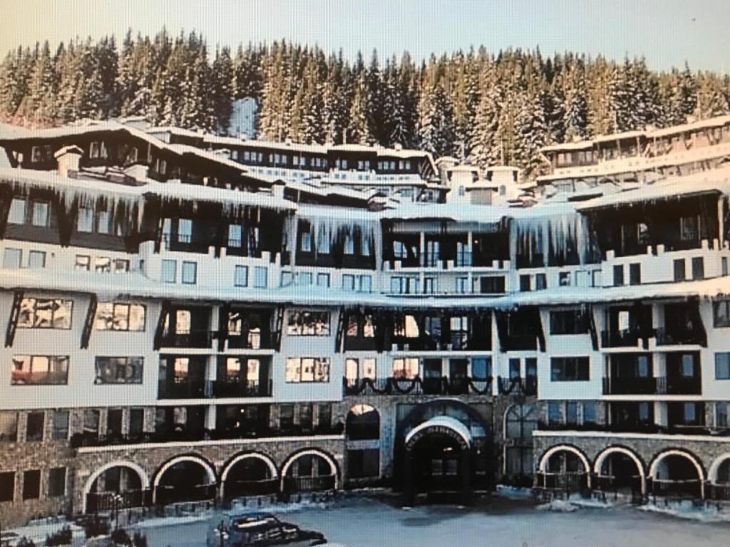 a building in the snow with trees in the background at Grand Monastery Apart-Hotel in Pamporovo