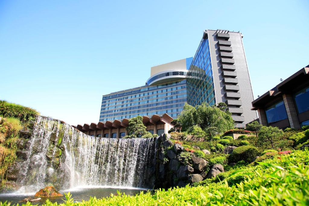 a waterfall in a garden with buildings in the background at Hotel New Otani Tokyo The Main in Tokyo