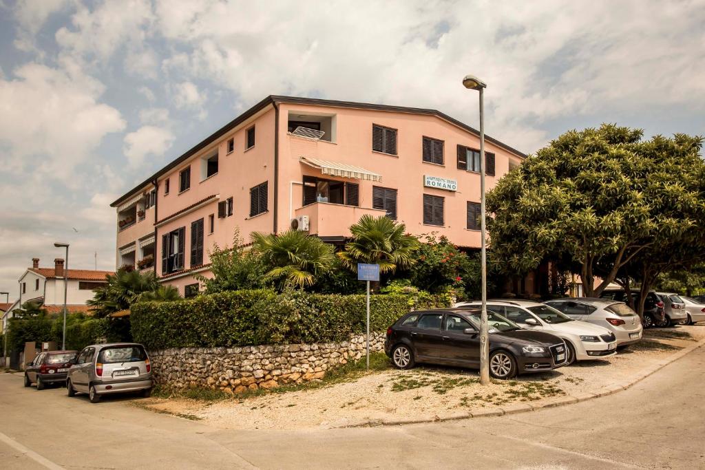 a pink building with cars parked in a parking lot at Apartments Romano in Rovinj