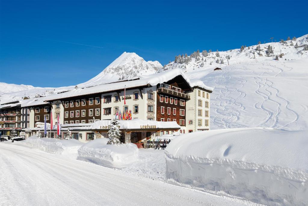 a building covered in snow next to a snow covered mountain at Sporthotel Lorünser in Zürs am Arlberg