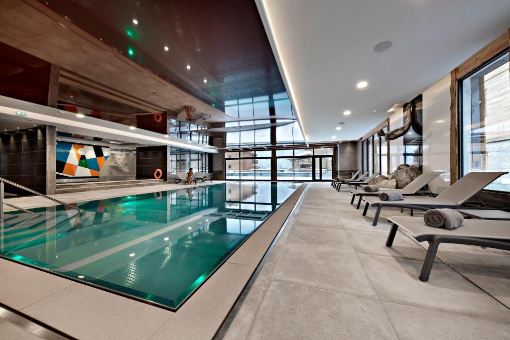 a large swimming pool in a building with chairs at Hôtel Alexane in Samoëns