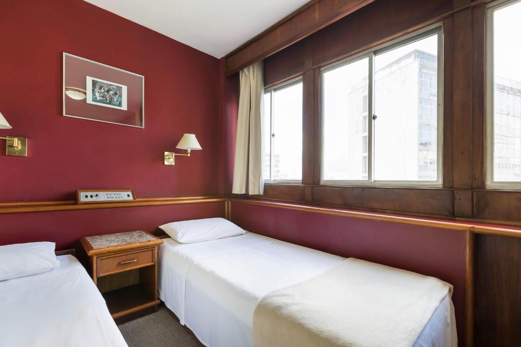two beds in a room with red walls and windows at Hotel Tibagi in Curitiba