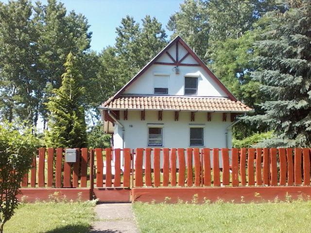 a small house with a red fence in front of it at Fácánkert Apartmanház in Tiszafüred