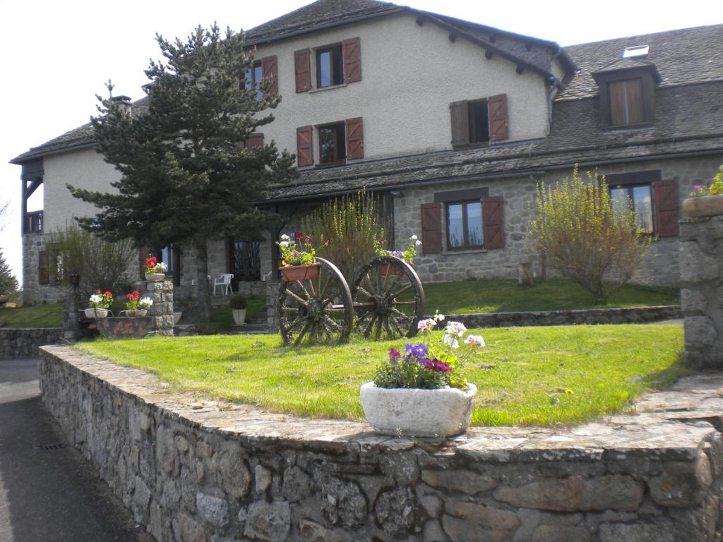 a stone wall in front of a house with flowers at Hôtel La Randonnée in Nasbinals