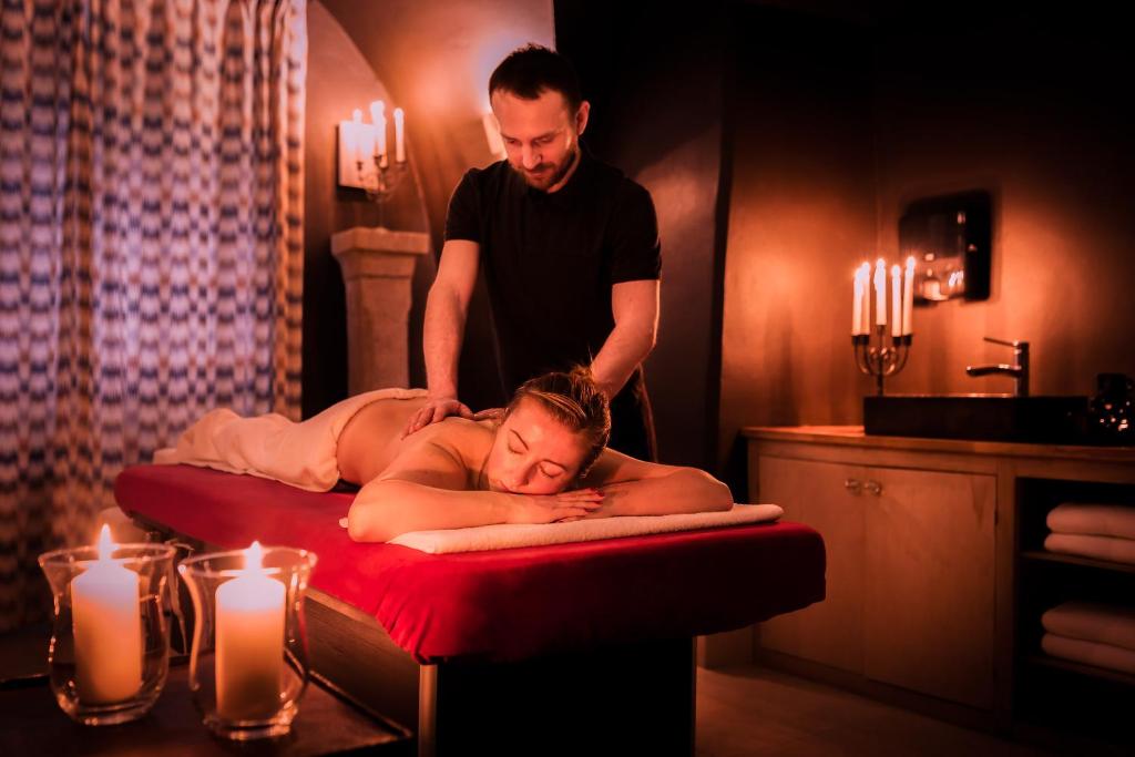 Therapist giving a calming massage to a relaxed client on red-covered table, candlelit spa ambiance.