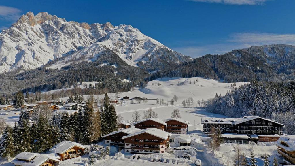 a ski lodge covered in snow with mountains in the background at Marco Polo Alpina Familien- & Sporthotel in Maria Alm am Steinernen Meer