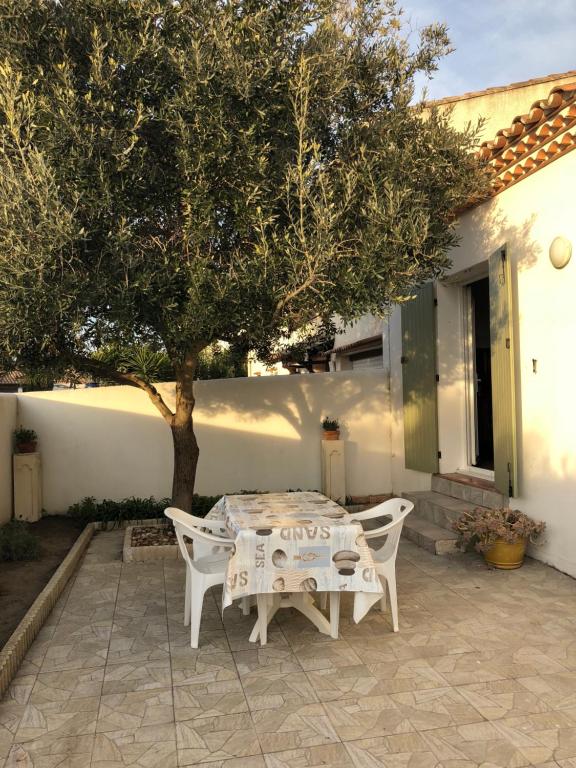 una mesa blanca y sillas bajo un árbol en un patio en Appartement de l'olivier, en Saintes-Maries-de-la-Mer