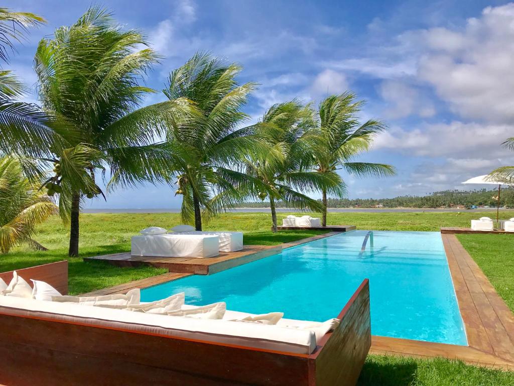 uma piscina com um barco em frente a algumas palmeiras em Pe na Areia Boutique Hotel em Japaratinga