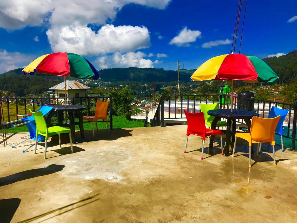 un patio con sillas coloridas, mesas y sombrillas en Loversleap bungalow en Nuwara Eliya