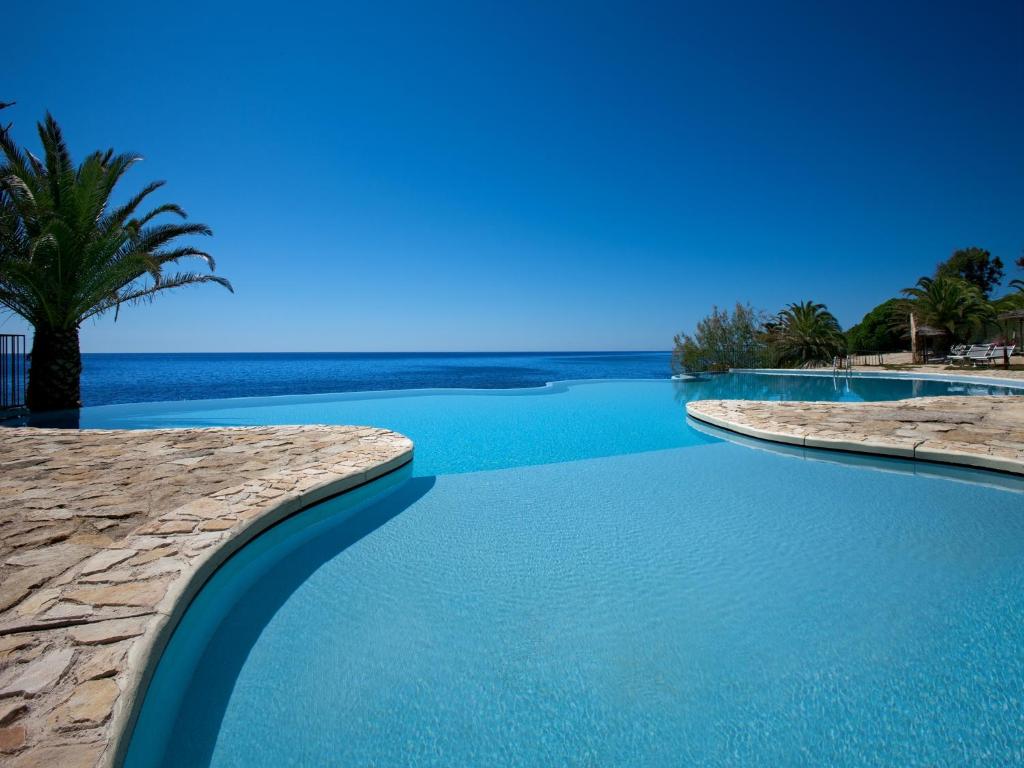 a swimming pool with blue water and a palm tree at Hotel Costa dei Fiori in Santa Margherita di Pula