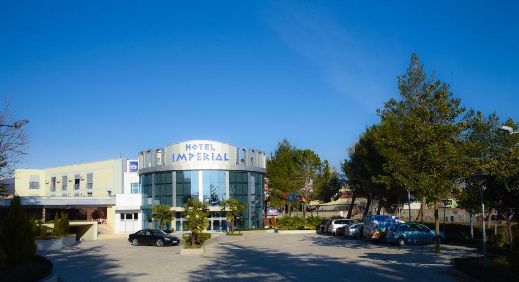 a large building with cars parked in a parking lot at Imperial Hotel IH in Elbasan